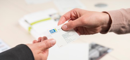 Das Bild zeigt, wie zwei Menschen eine Visitenkarte austauschen.